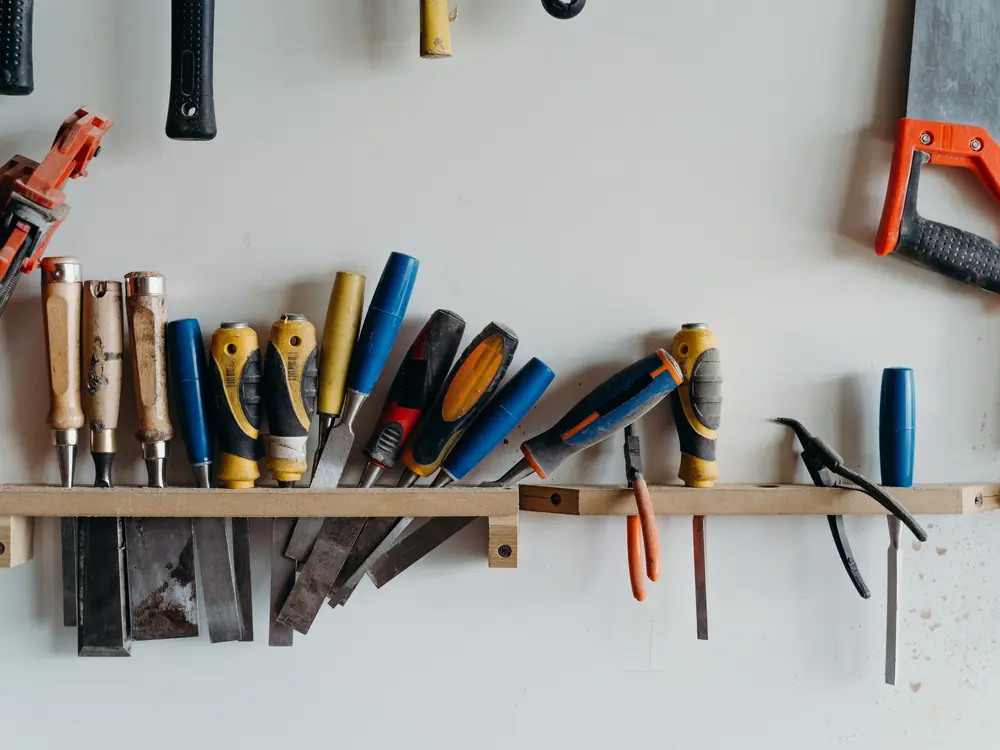 Chisels, screwdrivers, pliers and saws hanging on a wooden rack on a workshop wall.