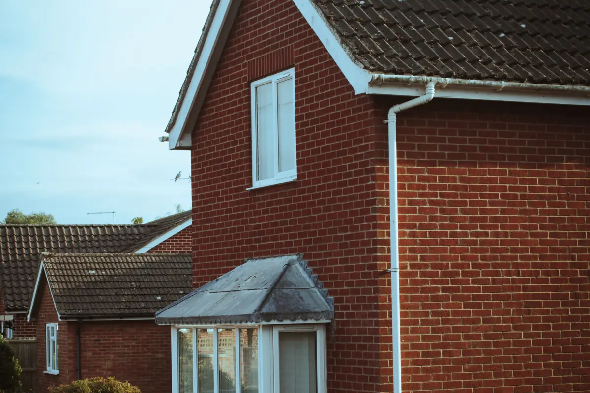 A red-brick house with white gutters, a downpipe and a bay window.