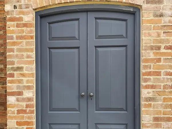 Grey painted double doors set in a brick arch.