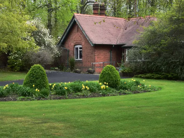 A mown lawn and a freshly edged flower bed with two clipped shrubs in front of a red-brick house.